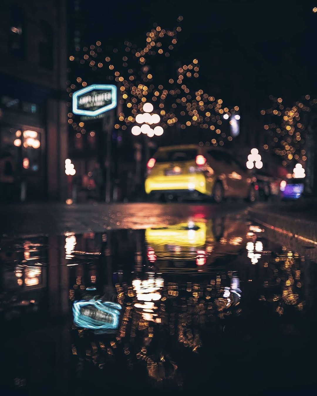 Neon sign and a yellow car reflected in a rain-soaked Vancouver street at night