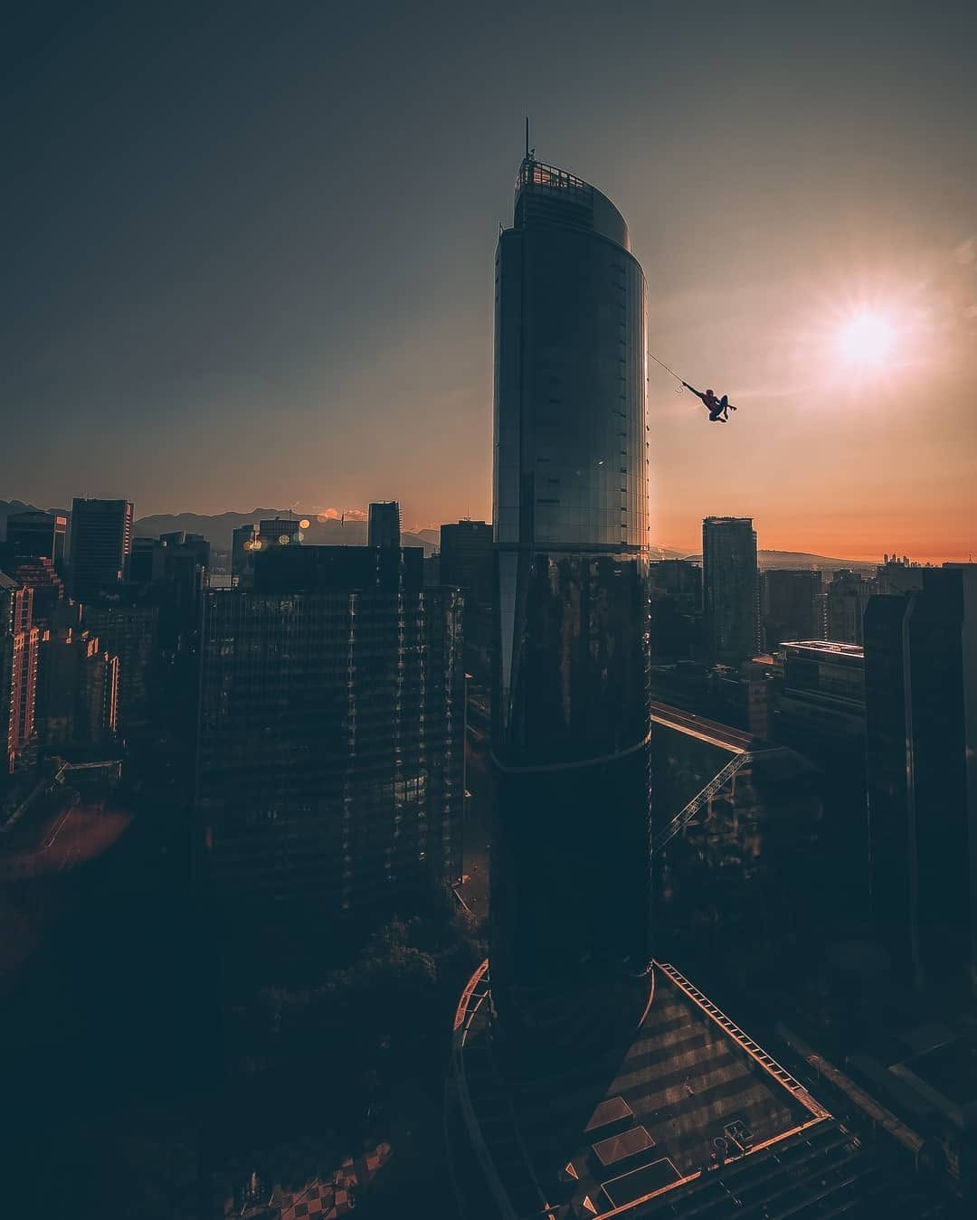 Silhouetted figure swinging past a glass Vancouver skyscraper at sunset