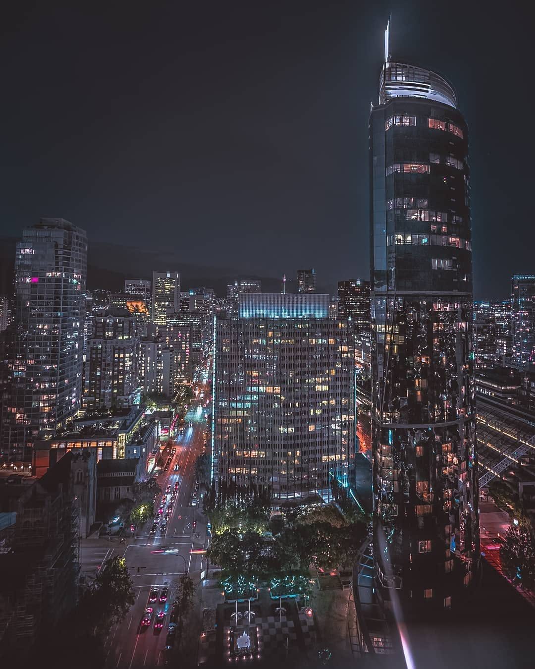 Reflective glass skyscraper glowing above Vancouver's night streets
