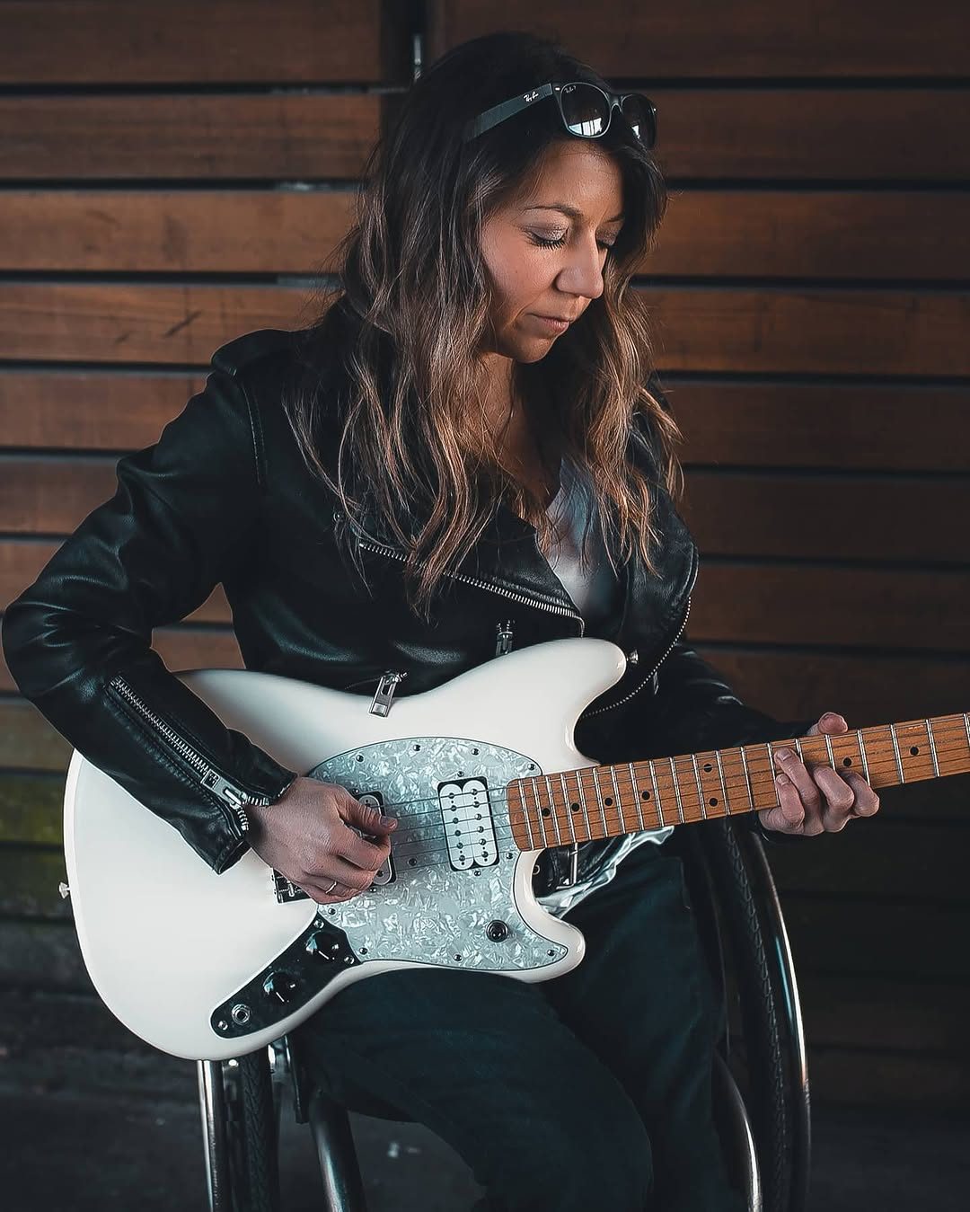 Portrait of a guitarist in a leather jacket, warm light against a wood-plank wall
