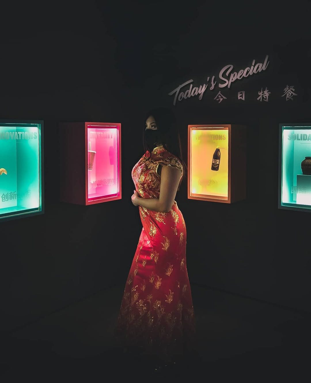 Moody portrait in a red embroidered qipao lit by glowing neon museum displays