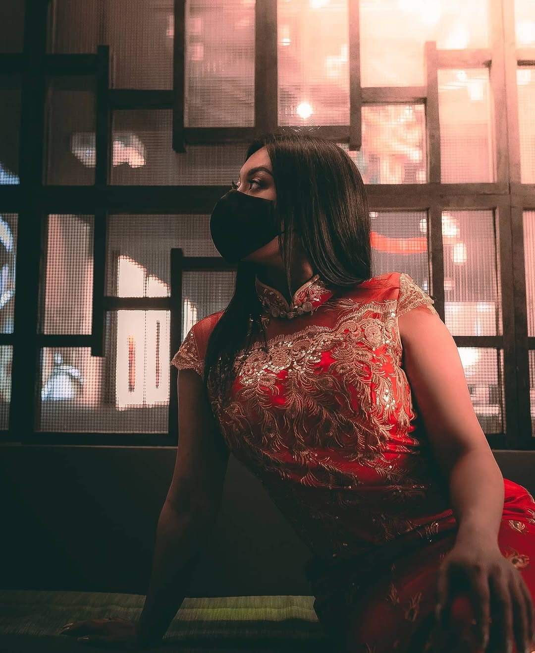 Profile portrait in a red and gold qipao, backlit by a warm lantern-lit window