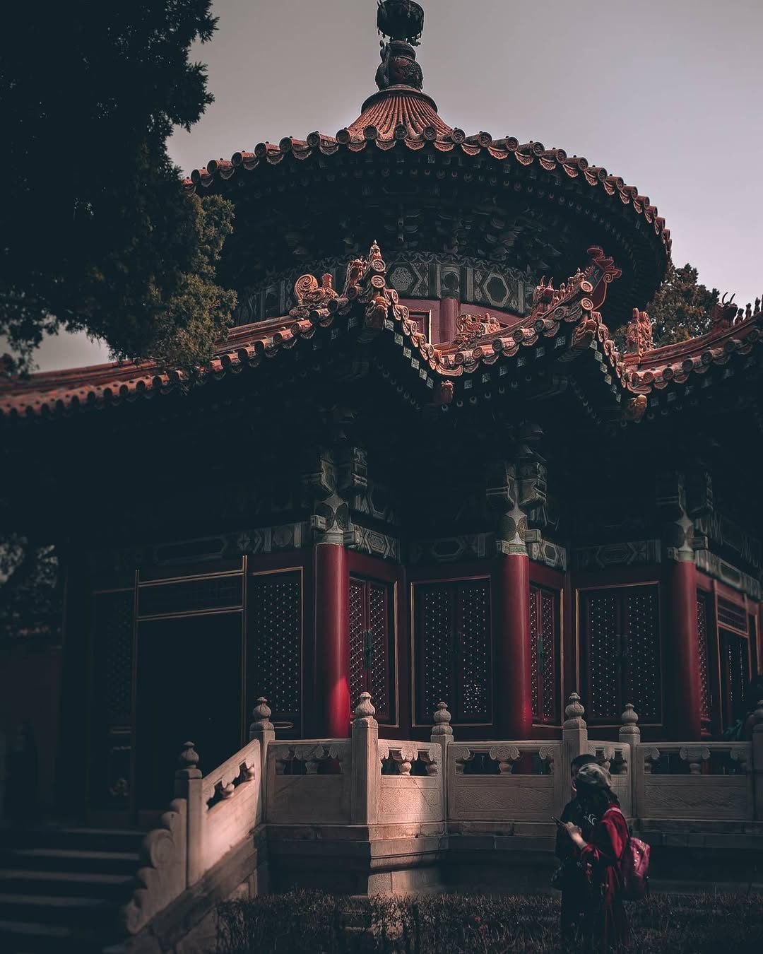 Figure in red beneath an ornate dark pavilion near Beijing's Forbidden City